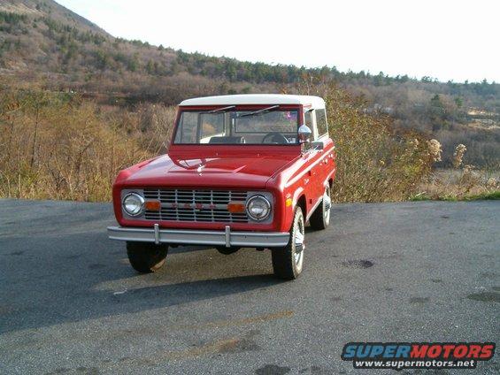 Red 1971 Ford Bronco parked on asphalt with a wooded hillside in the background