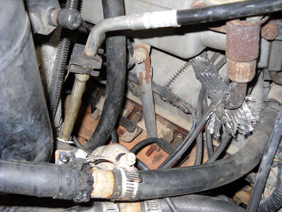 Engine compartment showing frayed wiring near exhaust pipe and various hoses