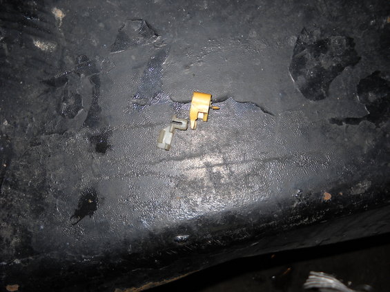 Close-up of a small plastic and metal door lock actuator component on a dark, textured surface