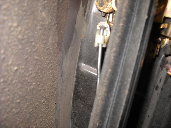 Close-up of a vehicle door lock mechanism with a metal rod and white plastic clip