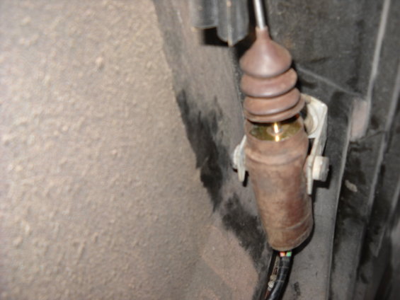 Close-up of a rusty door lock actuator cable with a rubber boot and metal housing