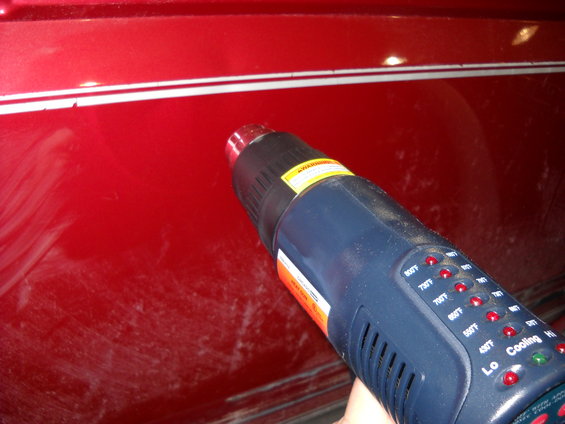 Heat gun pointed at a red car body panel with white pinstripes