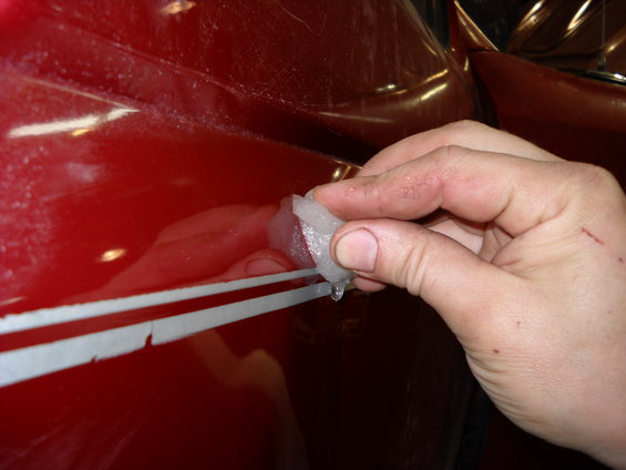 Hand removing white stripe decal from red vehicle side
