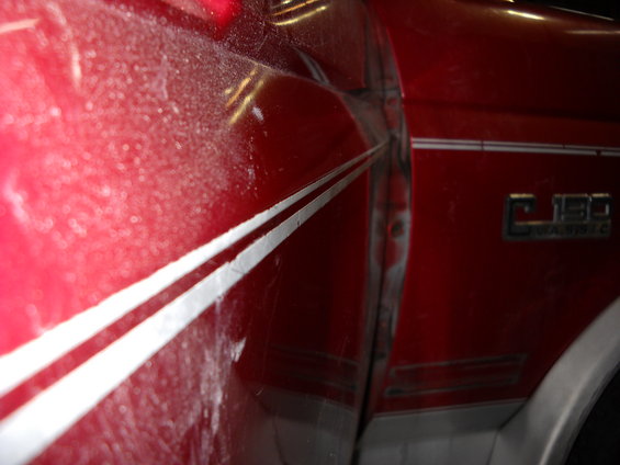 Red Ford F-150 pickup truck door with silver pinstripes and F-150 badge. Shows dust on the paint