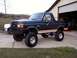 1990 Ford Bronco - A lifted Ford Bronco sits parked on a concrete driveway in front of an open garage door.