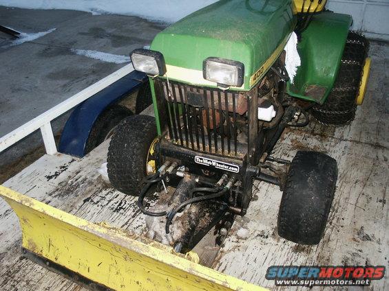 John Deere tractor with a yellow snow plow attached, sitting on a trailer