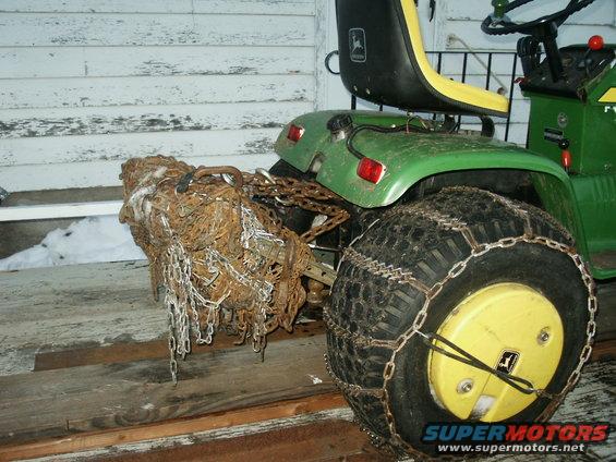 Green John Deere tractor rear with chains on tire and a pile of chains on the hitch