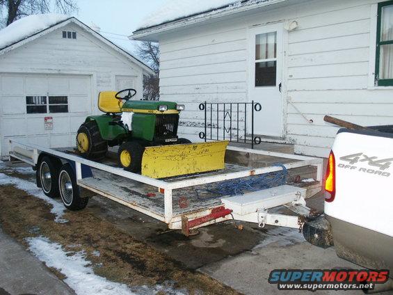 Green and yellow tractor with snow plow on trailer