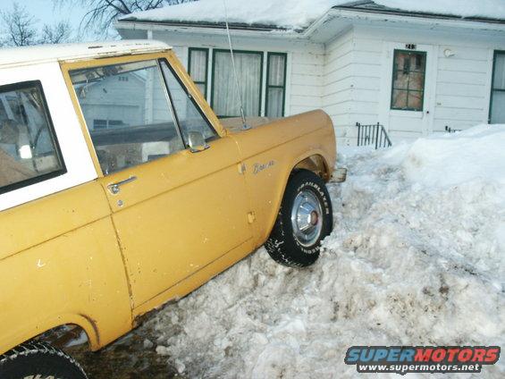 Yellow Ford Bronco parked in deep snow next to a white house