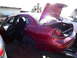 2003 Ford Taurus - A red sedan sits in a junkyard with its doors and trunk open, missing its wheels.