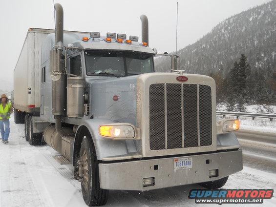 Peterbilt semi-truck and trailer on a snowy road, driver walking nearby
