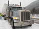 2009 Kenworth T800 - A Peterbilt semi-truck and trailer are parked on a snowy road with a driver standing next to it.