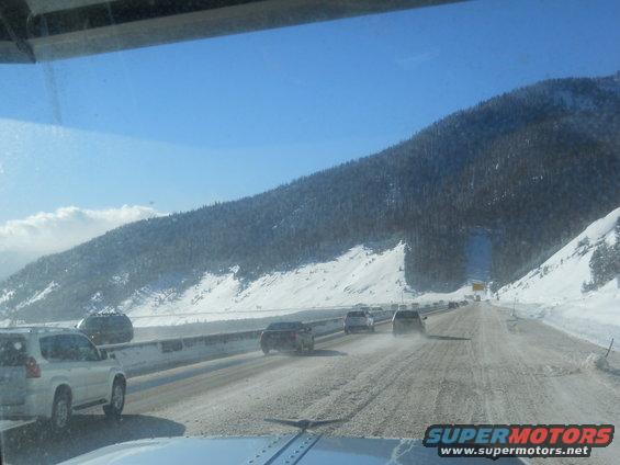 Traffic on a snow-covered highway with mountains and trees in the background