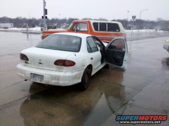 White sedan with doors open parked next to an orange SUV on a wet road