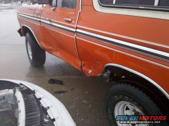 Side view of an orange SUV with significant body damage on the rear quarter panel and door