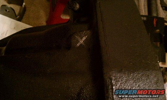 Black painted metal component with a white X scratched into its surface