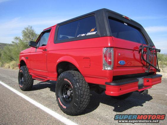 Red 1996 Ford Bronco with black top and off-road tires parked on the side of a road