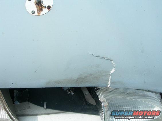 Close-up of a light blue vehicle hood with a scratch and a detached headlight assembly below