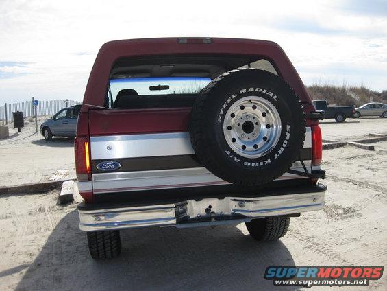 Red Ford Bronco with spare tire on rear, chrome bumper, and silver stripe