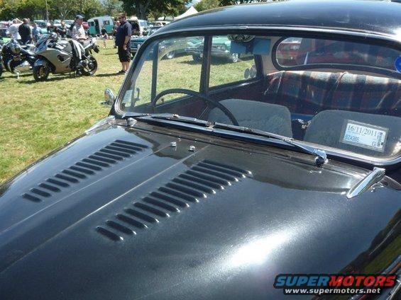 Black car hood with louvers, plaid interior, and a registration sticker on the windshield