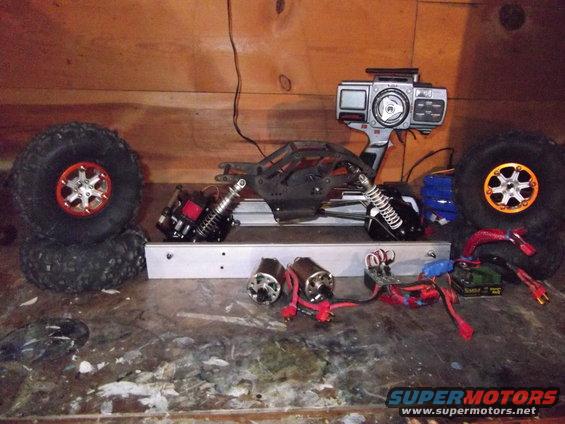 RC car chassis, two motors, shocks, tires, and remote control transmitter laid out on a workbench