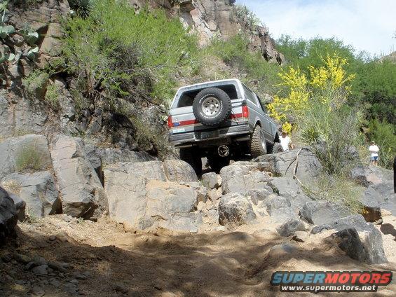 Silver Ford Bronco navigating a rocky trail with a spare tire on the back