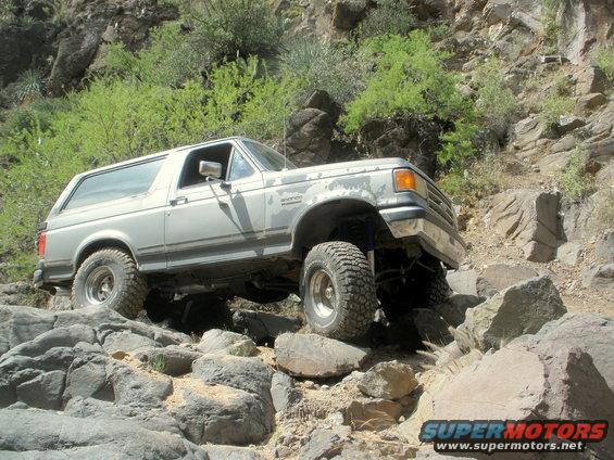 Silver Ford Bronco navigating rocky terrain, front-right tire elevated