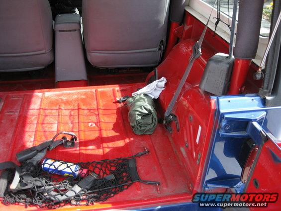 rear cargo area of a Jeep Wrangler with seats folded down, showing red floor, a rolled-up green bag, and a net with a bottle