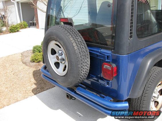 Blue Jeep Wrangler with spare tire mounted on rear door, aftermarket blue bumper