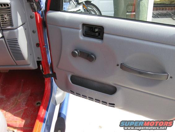 Gray interior door panel of a Jeep Wrangler with manual window crank, red floor visible