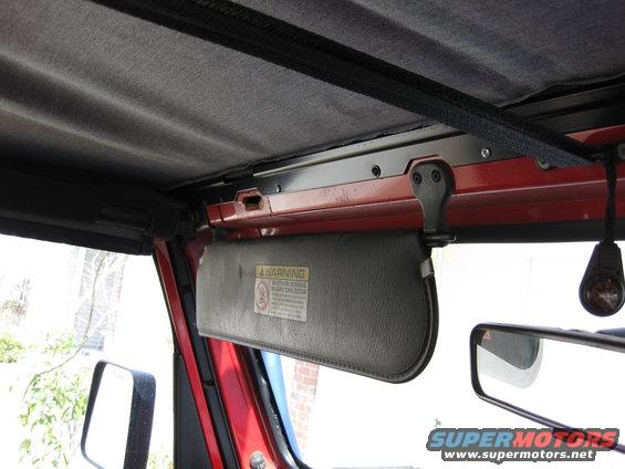 Interior of a red Jeep Wrangler showing the sun visor with a warning label and the side mirror