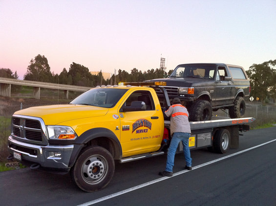 Tow truck loading a lifted black Ford Bronco onto its flatbed