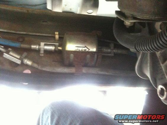Fuel filter with flow arrow visible, mounted on vehicle undercarriage