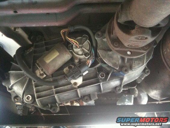 Transfer case with electrical connectors and driveshaft yoke. Visible text reads "SUPERMOTORS"