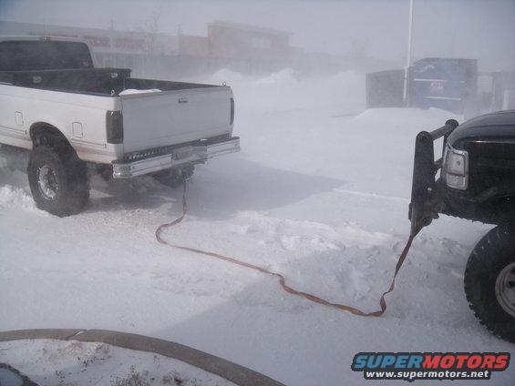 Two trucks connected by a tow strap in a snowy environment