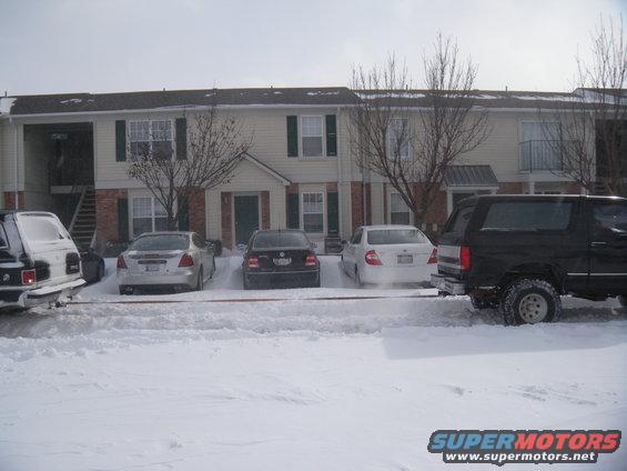 Black SUV with off-road tires parked in snow, other cars visible