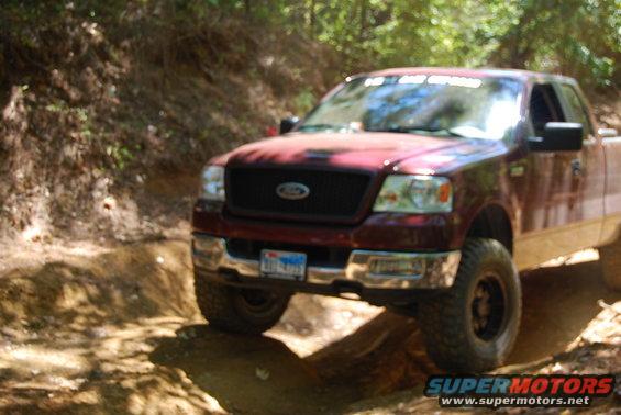 Maroon Ford F-150 truck driving on a dirt trail, front quarter view