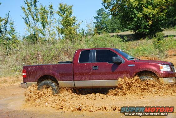 Red 2005 Ford F-150 driving through mud, splashing water