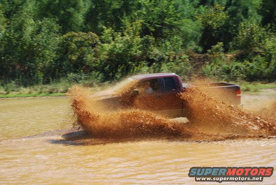 Truck driving through a mud puddle, kicking up a large spray of mud