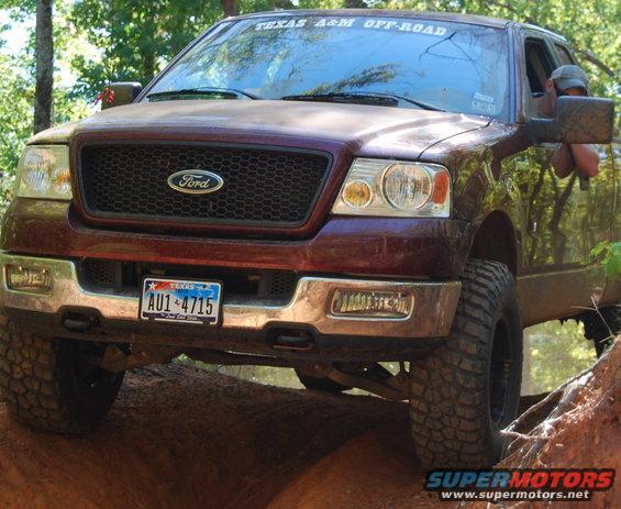 Maroon Ford F-150 truck with off-road tires on a dirt trail, front view