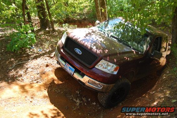 Maroon Ford F-150 driving on a dirt trail with trees around. License plate is visible