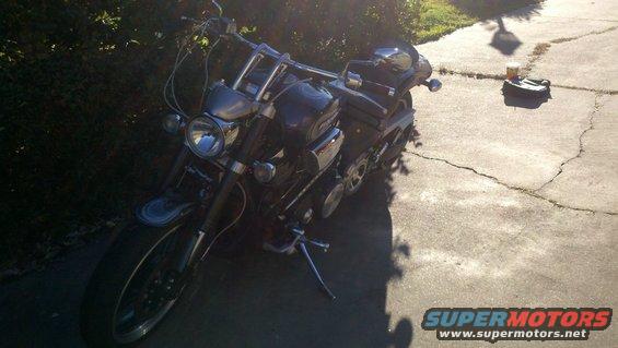 Dark motorcycle parked on cracked concrete, front 3/4 view