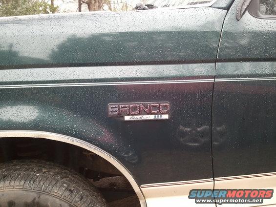 Green 1993 Ford Bronco Eddie Bauer side badge with water droplets, showing part of the front fender and tire