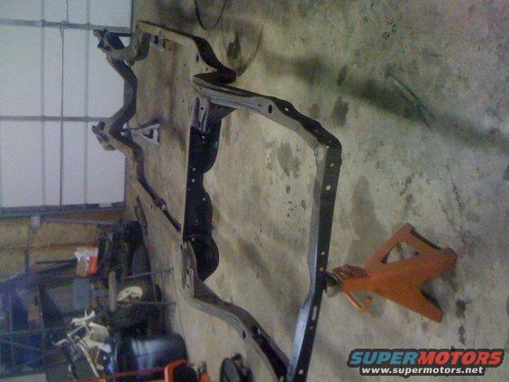 Black metal vehicle frame on an orange jack stand against a concrete wall