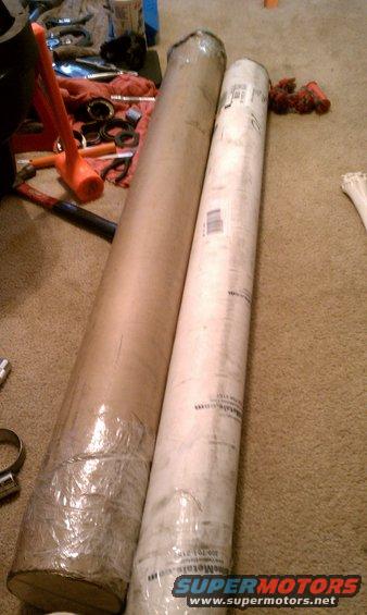Two large rolled up items, one in brown paper and one in white paper, sit on a carpeted floor next to tools including a rubber mallet