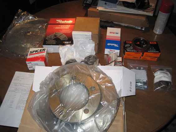 Various new brake rotors, pads, and bearings laid out on a table. Boxes show brands like Spicer, Raybestos, and Timken