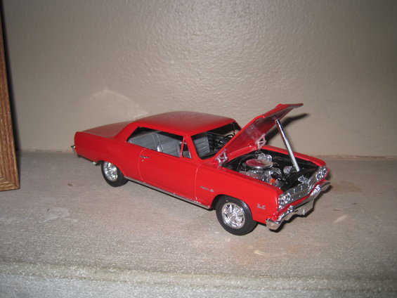 Red model car, possibly a 1960s Chevrolet, with hood open showing engine detail