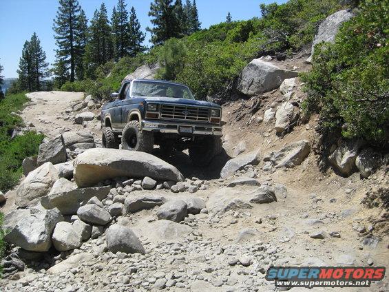 1986 Ford Bronco navigating a steep, rocky off-road trail with large boulders