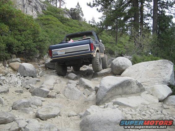 Dark blue Ford Bronco with silver trim driving over rocks on a dirt trail
