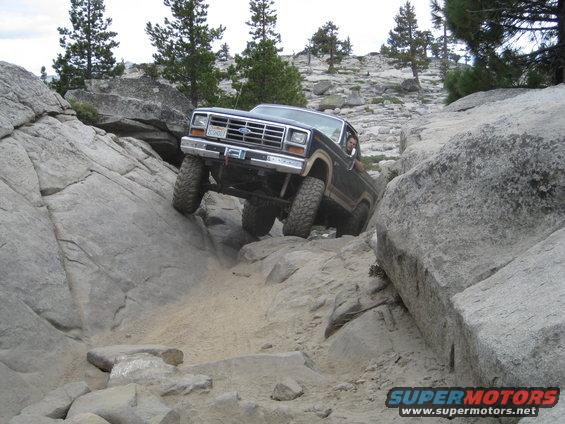 Ford Bronco climbing over rocks on a trail. Driver visible